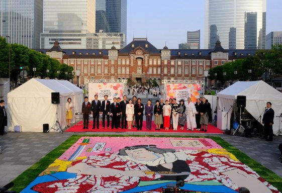 Evento al aire libre con un gran mural, carpas y un grupo de personas posando.
