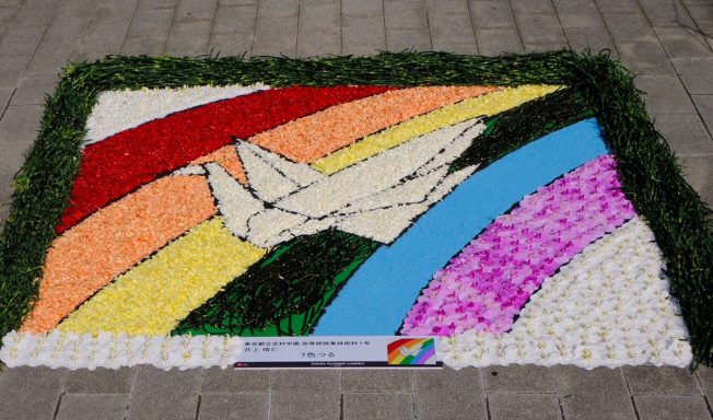 Mural colorido con un barco de papel y arcosíris, hecho con flores y pétalos.